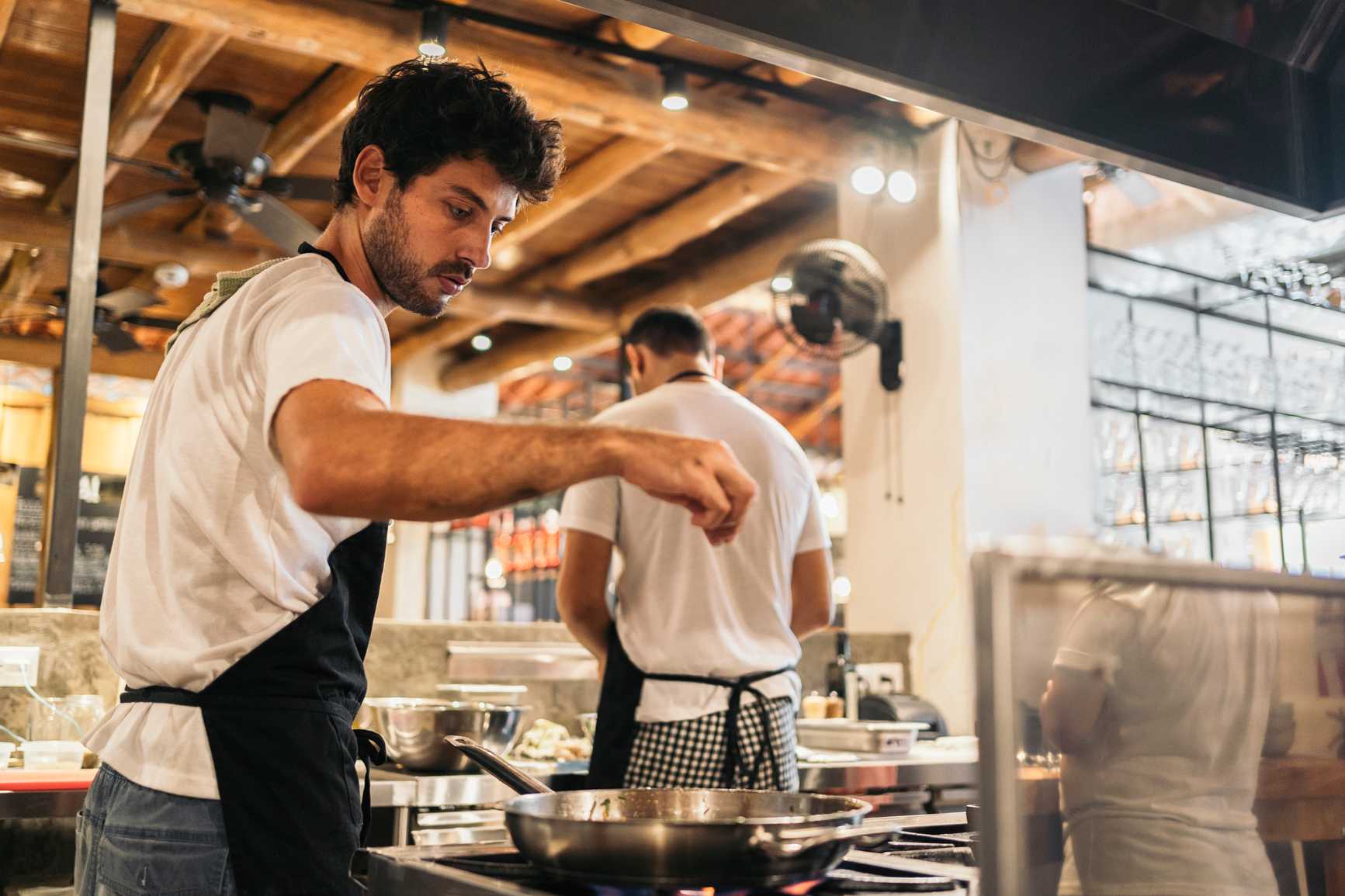 Stock photo of professional chef wearing apron cooking in restaurant and using saucepan.