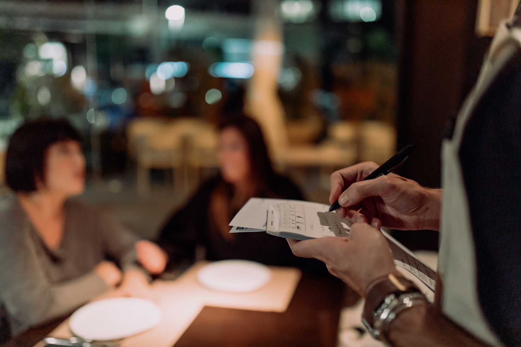 Spanish waitress takes order in restaurant using note and pen writing standing talking with client in restaurant